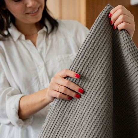 Woman holding classic style waffle bath mat in stone.