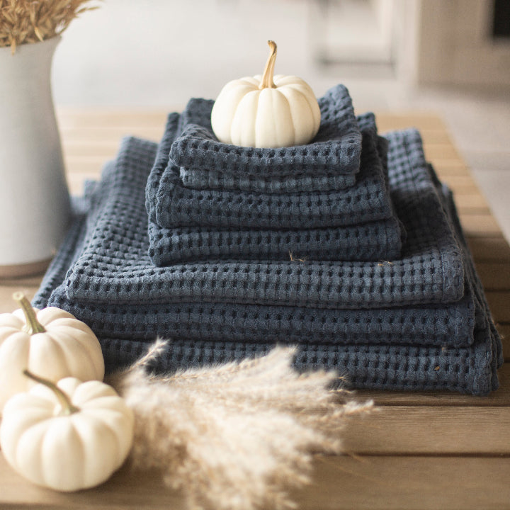 Stack of blue towels on a wooden surface with white pumpkins and decorative elements.