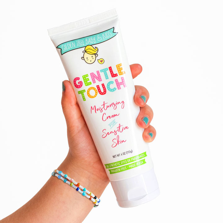 A hand with teal nail polish holds a white tube of Gentle Touch Moisturizing Cream for Sensitive Skin against a clean white background.
